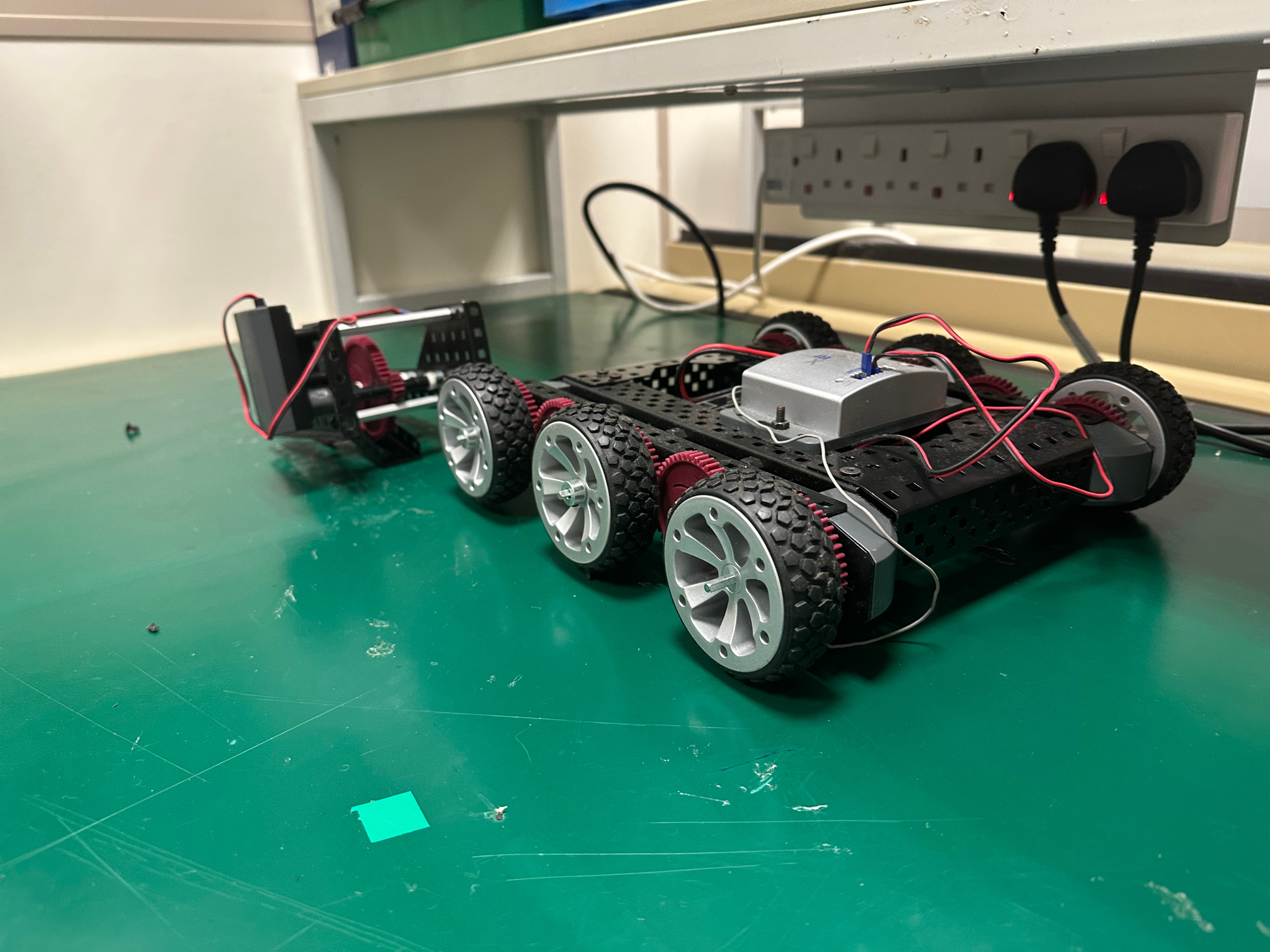 A robot on a table that has 6 wheels and a claw.