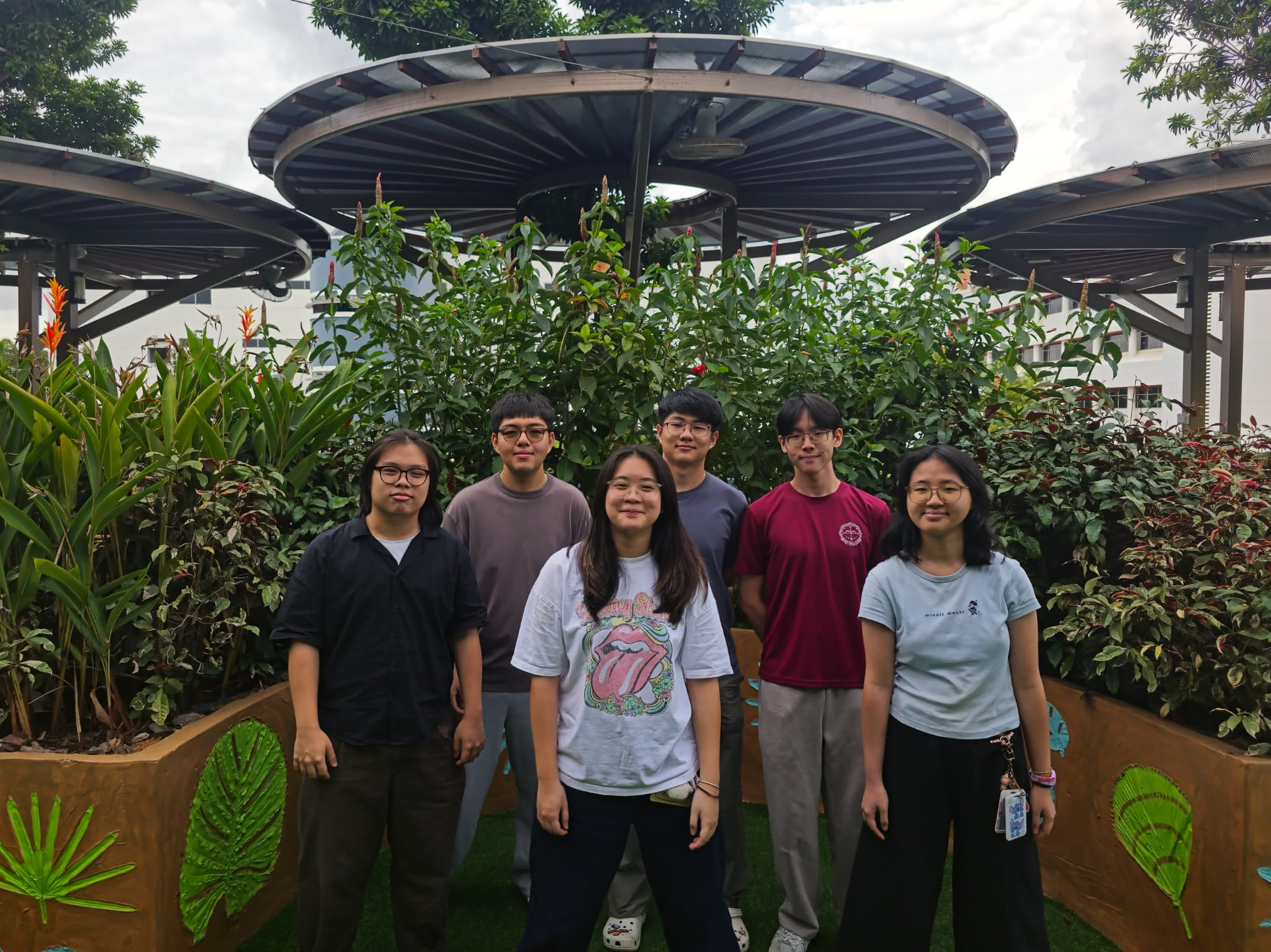 A group portrait of about eight students standing together in a lush, outdoor courtyard or courtyard setting.